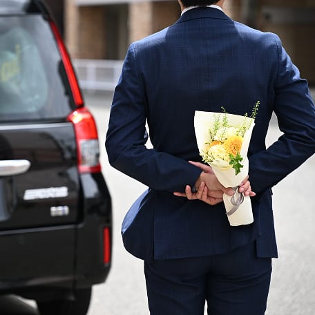 花束を後ろ手に持ち立つスーツ姿の男性