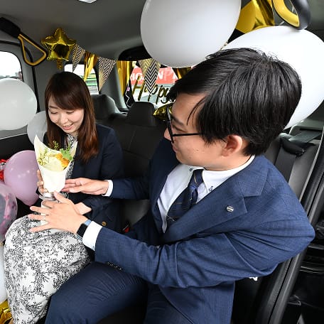 サプライズタクシー内で女性のお客様に花束を渡しているスーツの男性